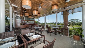 Un espace extérieur aménagé pour les repas, avec des meubles en osier, des ventilateurs de plafond et une vue sur le paysage.