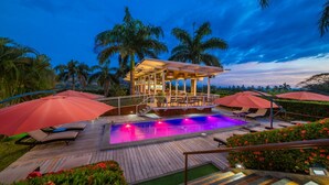 A pool area with lounge chairs and umbrellas, surrounded by palm trees and a covered seating area. - Hotel Palma de Oro (Bejuco)