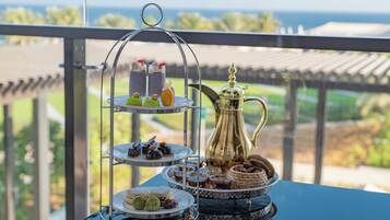 A tiered dessert stand with various sweets and a decorative pitcher on a table with a view of the outdoors.