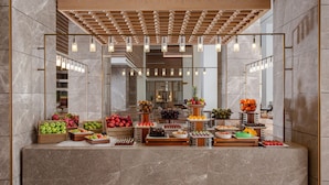 A modern hotel lobby with a marble reception desk, wooden accents, and a variety of fruits and desserts displayed. - InterContinental Fujairah Resort by IHG (Al Aqah)