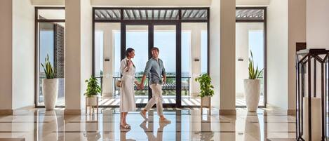 A modern hotel lobby with a reflective floor, large windows, and potted plants.