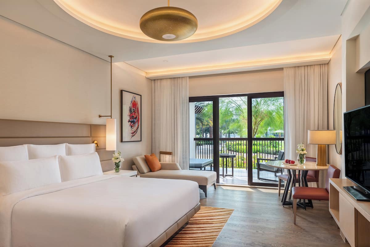 Habitación de hotel moderna con una cama grande, un escritorio, televisión y un balcón con mobiliario exterior.