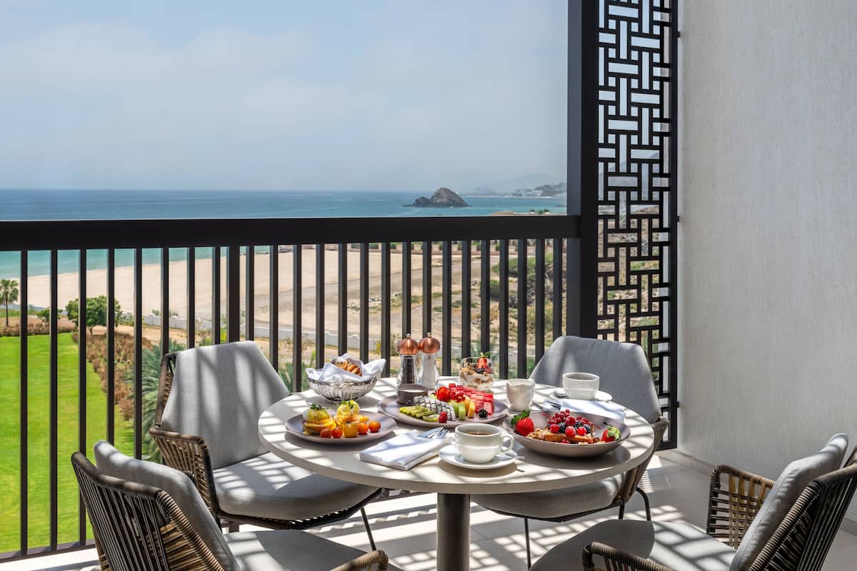 Un balcón con una mesa lista para el desayuno, con vista a una playa y un campo de golf.