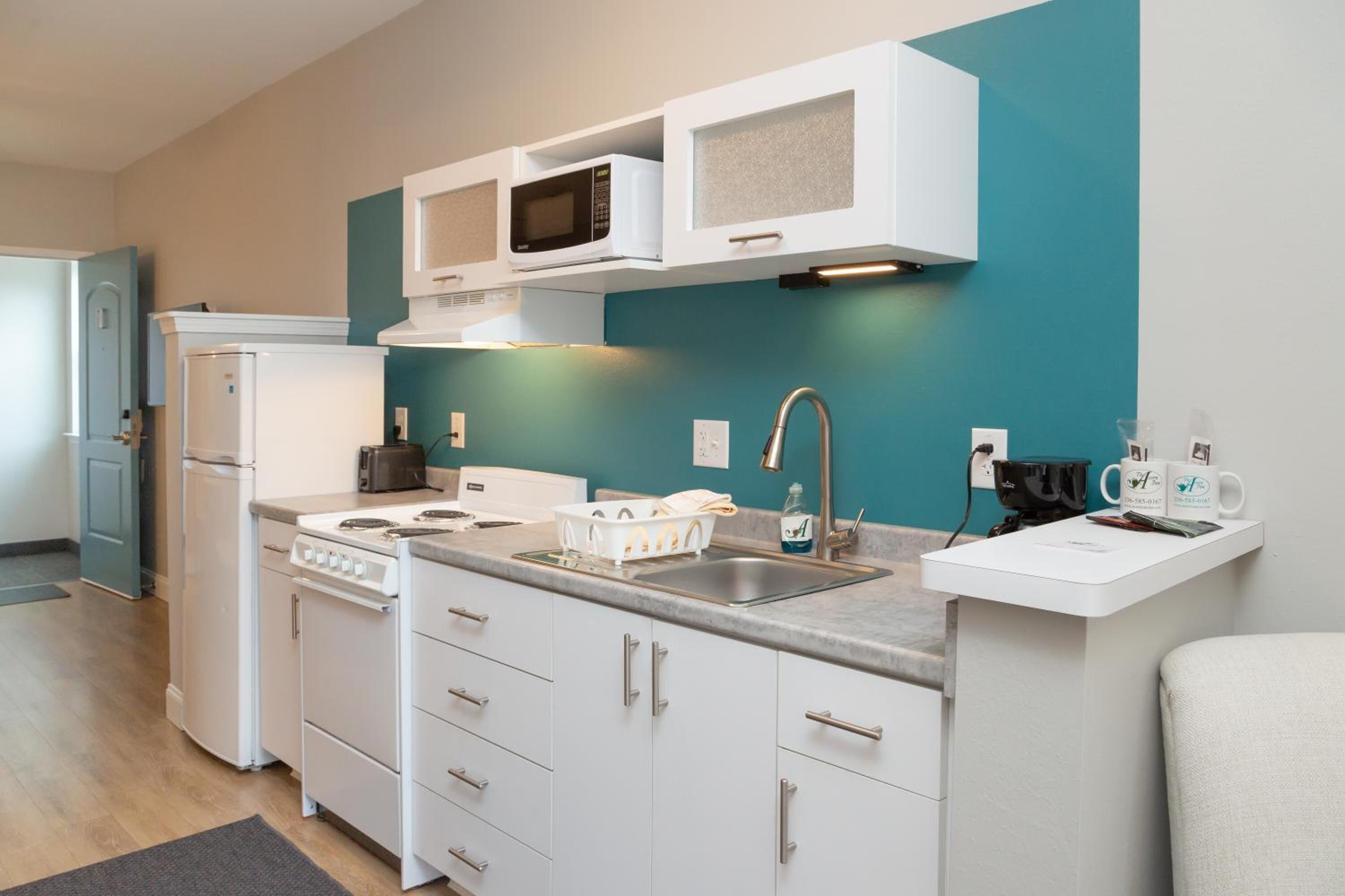 A compact kitchen with white cabinets, a stove, a microwave, and a sink.