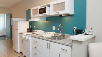 A compact kitchen with white cabinets, a stove, a microwave, and a sink.