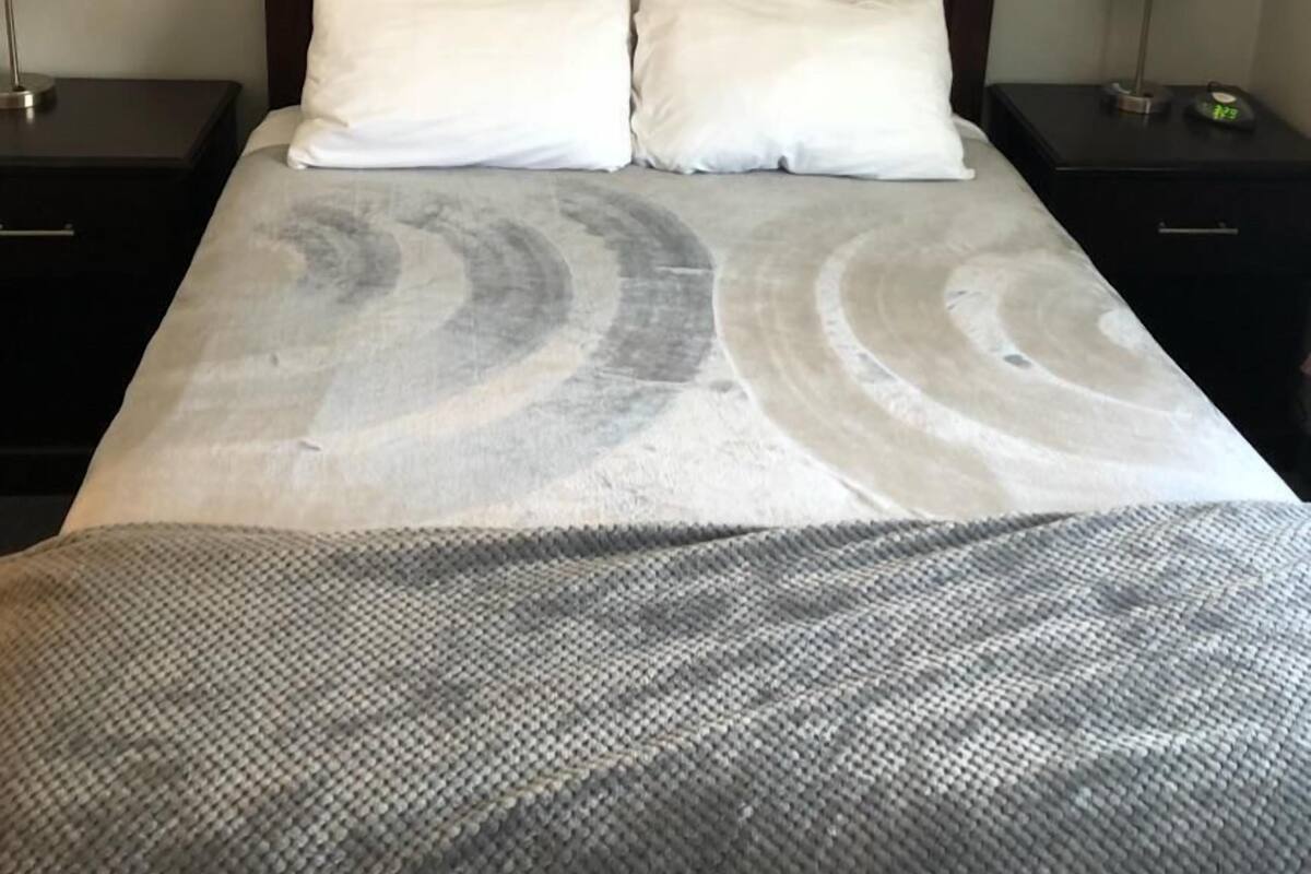 A hotel room with a large bed, two bedside tables with lamps, a modern abstract painting on the wall, and a patterned bedspread.