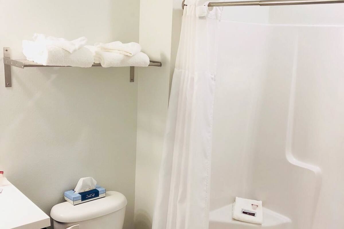 A bathroom with a toilet, a sink, a shower with a curtain, and a shelf with towels.