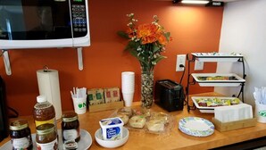Uma bancada de cozinha com diversos alimentos, um micro-ondas, um vaso com flores e uma cafeteira.