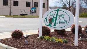 Placa de The Acorn Suites com um edifício moderno ao fundo.