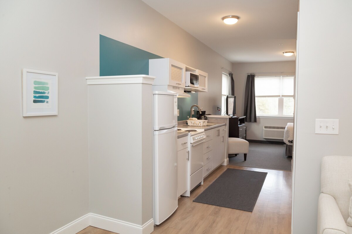 A modern kitchen with white appliances, a grey rug, and a view to the living area.
