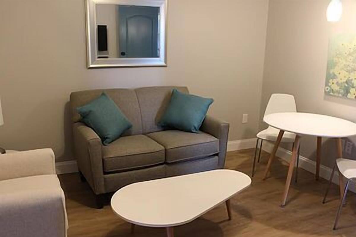 A living room with a grey sofa, two teal cushions, a white coffee table, and a white round table with four chairs.