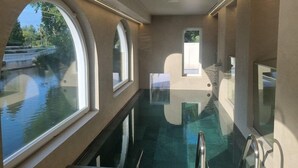A pool area with clear glass walls and windows, a metal ladder, and a view of a water body outside. - Estalagem De Santa Iria (Tomar)