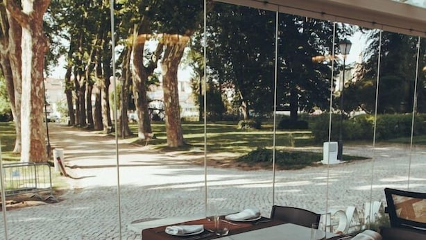 An outdoor dining area with tables and chairs, a glass enclosure, and a view of trees and a pathway. - Estalagem De Santa Iria (Tomar)