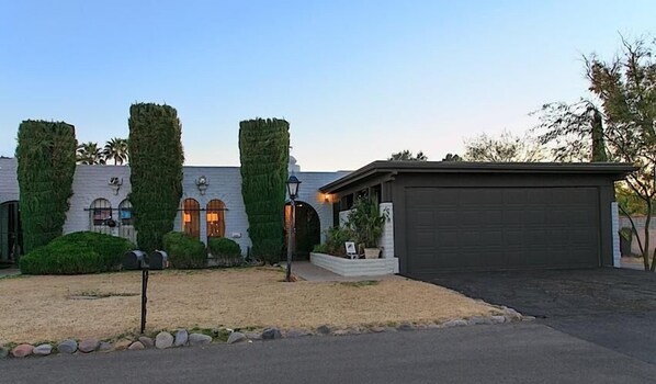 A residential property with a garage, a landscaped front yard, and a building with a stone facade. - La Vida Local By Signature Vacation Rentals (Tucson)