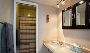 A bathroom with a striped shower curtain, a wooden towel rack, a mirror, and a sink with toiletries. - La Vida Local By Signature Vacation Rentals (Tucson)