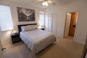 A bedroom with a bed, nightstands, a ceiling fan, a painting, and a door leading to another room. - Kierland Villa By Signature Vacation Rentals (Scottsdale)