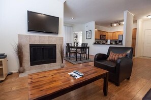 A modern living room with a fireplace, a flat-screen TV mounted above it, a dining area with a table and chairs, and a kitchen visible in the background. - Kierland Villa By Signature Vacation Rentals (Scottsdale)