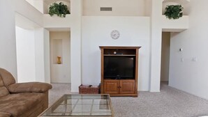 A living room with a brown sofa, a glass-top coffee table, a wooden entertainment unit with a TV, and a clock on the wall. - Keep It Simple By Signature Vacation Rentals (Glendale)