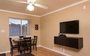 A room with a dining table and chairs, a ceiling fan, a mounted TV, and a window with blinds. - Just Darling By Signature Vacation Rentals (Phoenix)