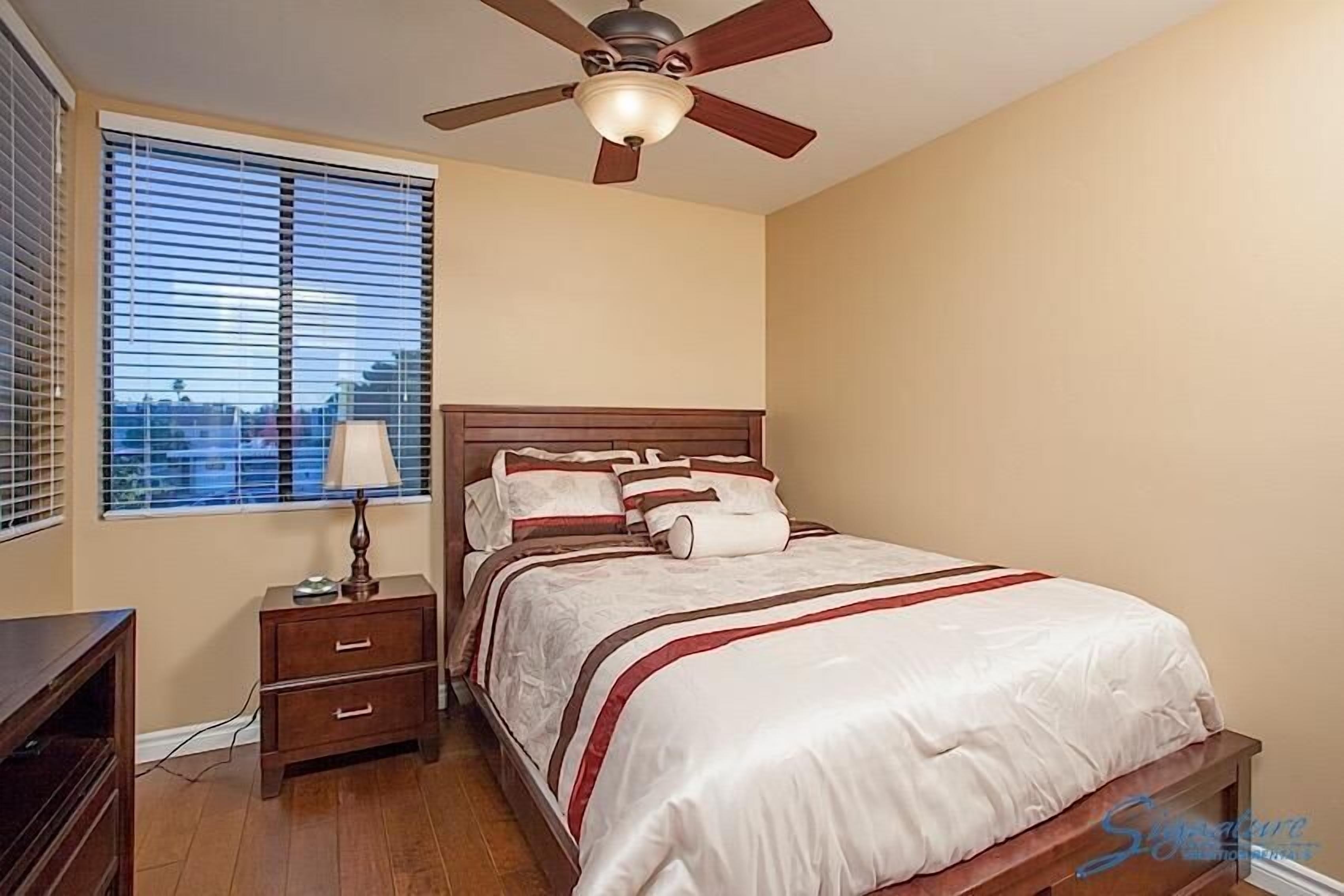 Une chambre à coucher avec un lit, une table de chevet, une lampe et un ventilateur de plafond.