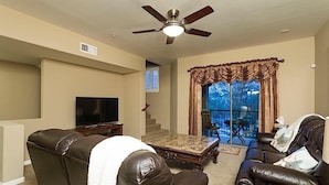 A living room with a ceiling fan, a flat-screen TV, leather sofas, and a large window with curtains. - Hot Spot at Desert Ridge By Signature Vacation R (Phoenix)