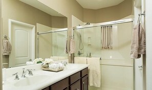 A bathroom with a large mirror, a glass-enclosed shower, a white sink with two faucets, and a vanity with dark cabinets.