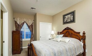 A bedroom with a wooden bed, a dresser, a window with curtains, a door, and a framed picture on the wall.