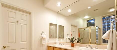 A bathroom with a double sink, wooden cabinets, a large mirror, and a potted plant.