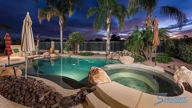 A pool area with a hot tub, palm trees, and lounge chairs. - Hole in One By Signature Vacation Rentals (Goodyear)