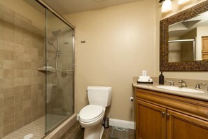 A bathroom with a glass-enclosed shower, a white toilet, and a wooden vanity with a mirror. - Hidden Oasis By Signature Vacation Rentals (Glendale)