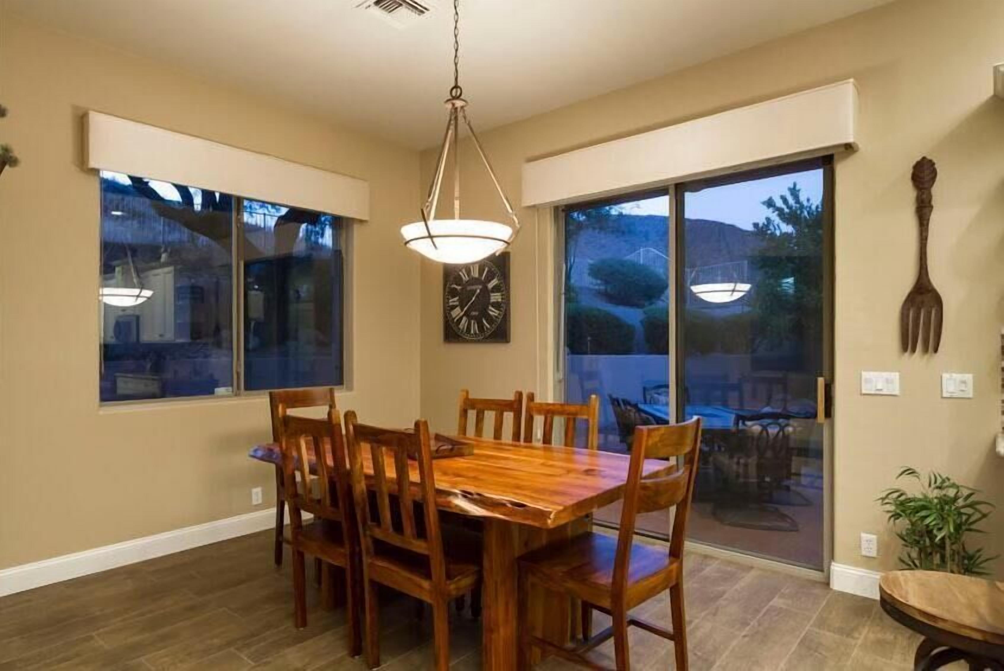 A dining area with a wooden table and chairs, large windows, and a hanging light fixture.