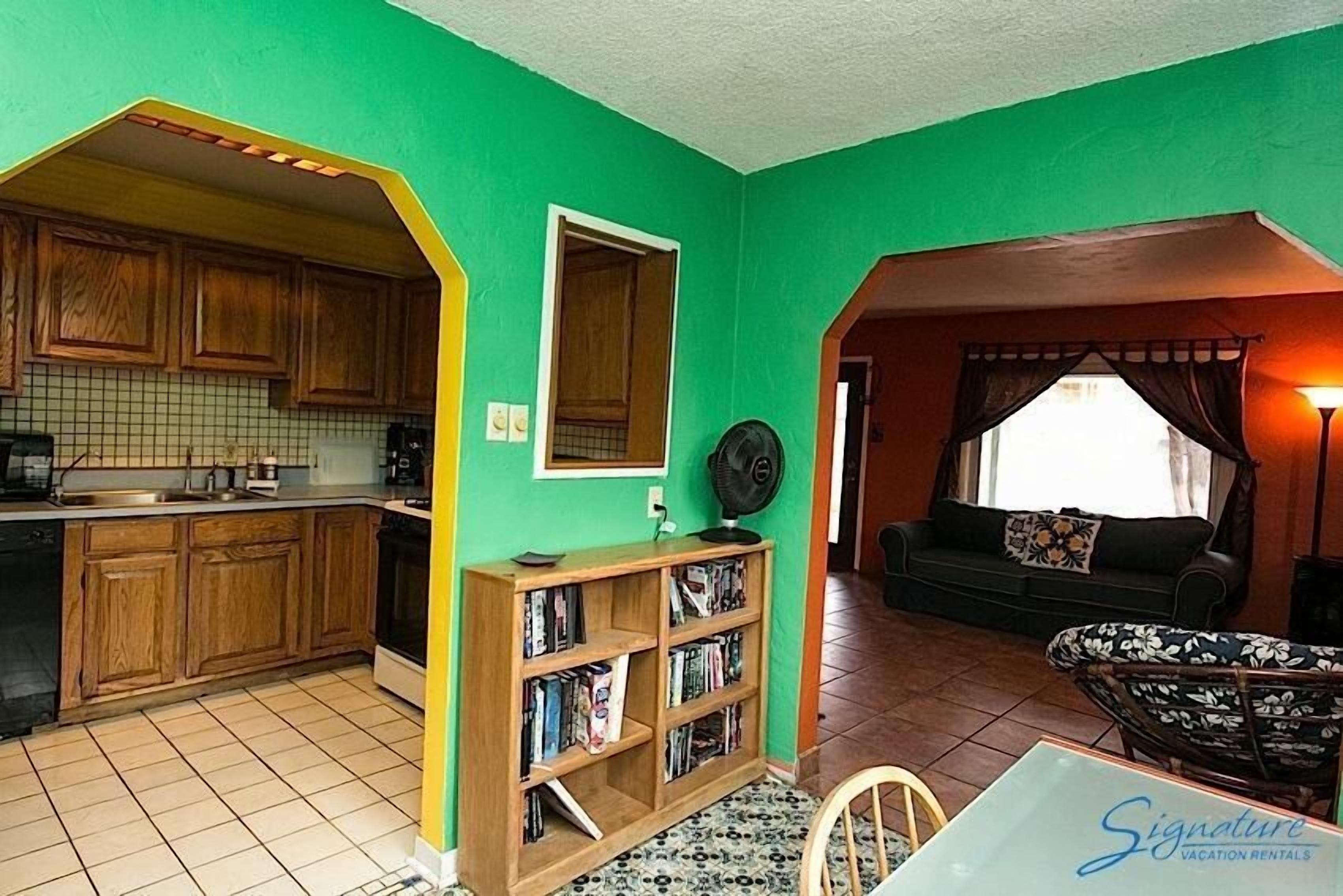 A compact living space with a kitchen, a bookshelf, a dining area, and a seating area with a sofa and chairs.