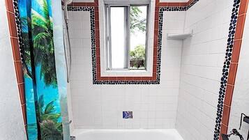 Un baño con bañera, ducha y ventana con vistas al paisaje verde exterior.