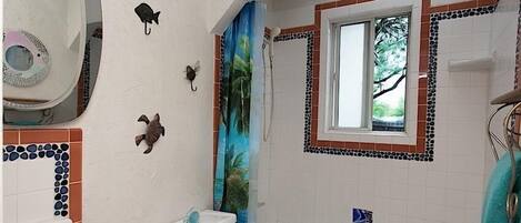 A bathroom with a toilet, sink, bathtub, and shower. There are decorative tiles on the walls and a window with a view of trees.