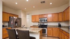 Una cocina con armarios de madera, un refrigerador, un microondas, un horno y una encimera de granito.