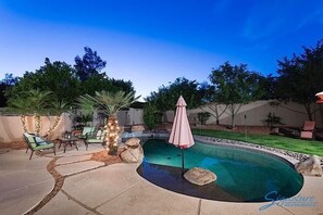 Un patio trasero con piscina, muebles de jardín y un pequeño jardín.