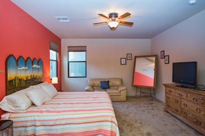 Een slaapkamer met een bed, een plafondventilator, een dressoir, een televisietoestel en een schilderij aan de muur.