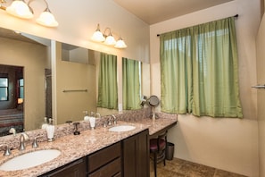Un baño con dos lavamanos, un espejo grande y cortinas verdes.