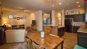 A spacious living area with a wooden dining table, a sofa, and a TV. There is a kitchen area with dark cabinets and a refrigerator. - Heart of Tucson By Signature Vacation Rentals (Tucson)