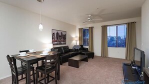 Ein modernes Wohnzimmer mit einem Esstisch, gedeckt für vier Personen, einer schwarzen Ledersofa, einem Deckenventilator und einem großen Fenster mit Vorhängen.