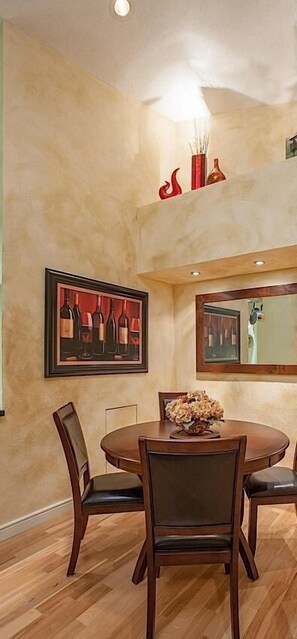 A dining area with a round table, four chairs, a vase of flowers, and two framed artworks on the wall. - Happy Ours By Signature Vacation Rentals (Paradise Valley)