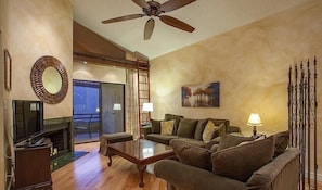 A living room with a sofa, a coffee table, a TV, and a ceiling fan. - Happy Ours By Signature Vacation Rentals (Paradise Valley)