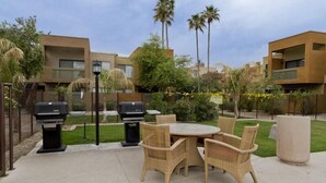 An outdoor patio area with wicker furniture, two barbecue grills, and a round table. - Hangout By Signature Vacation Rentals (Scottsdale)