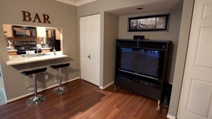 A compact kitchen with a microwave, stove, and bar stools. A flat-screen TV is mounted above a dark entertainment unit. - Hangout By Signature Vacation Rentals (Scottsdale)