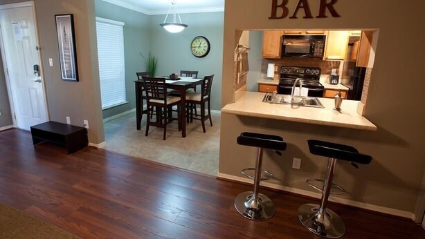 A compact kitchen with a bar area, wooden flooring, and a dining area with a table and chairs. - Hangout By Signature Vacation Rentals (Scottsdale)
