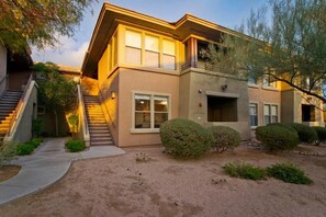 A two-story building with a staircase leading to the entrance, surrounded by landscaped greenery and a clear sky. - Grayhawk Villa Del Sol By Signature Vacation Rental (Scottsdale)