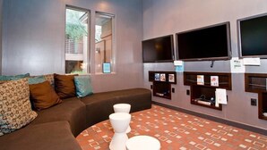 Une salle de bain moderne avec un canapé marron, trois toilettes blanches et deux téléviseurs fixés au mur.