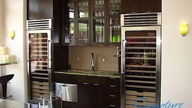 Cozinha moderna com armários de madeira escura, eletrodomésticos de aço inoxidável e painel de vidro.