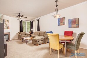 A living room with a sofa, a coffee table, a TV, a ceiling fan, and a dining area with chairs and a table.