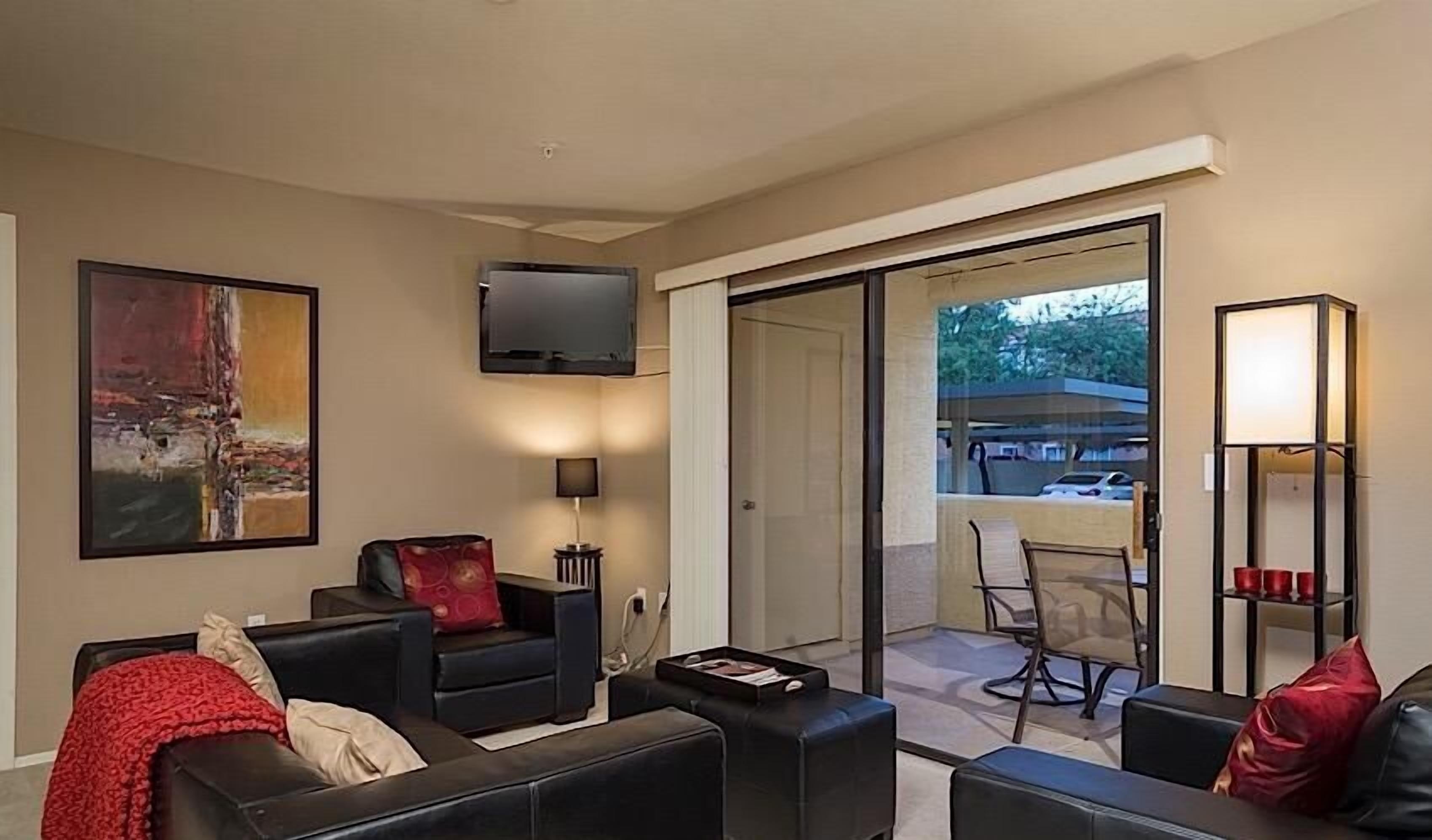 A modern living room with a flat-screen TV, a painting, and a dining area with chairs and a table.